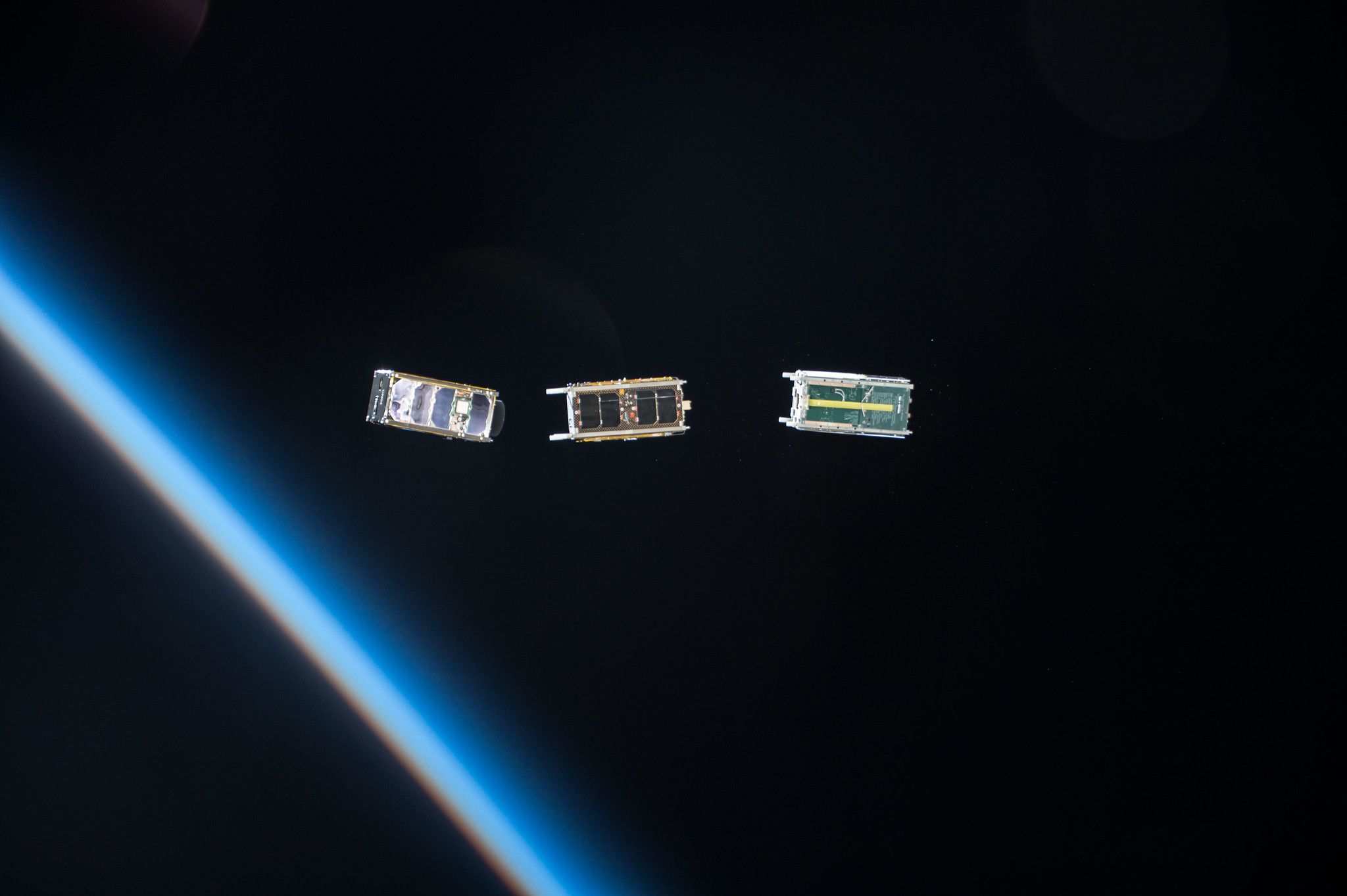 Tre CubeSat appena rilasciati dal modulo Kibo della ISS, con l’atmosfera terrestre sullo sfondo, per studiare lo spazio vicino e il clima spaziale